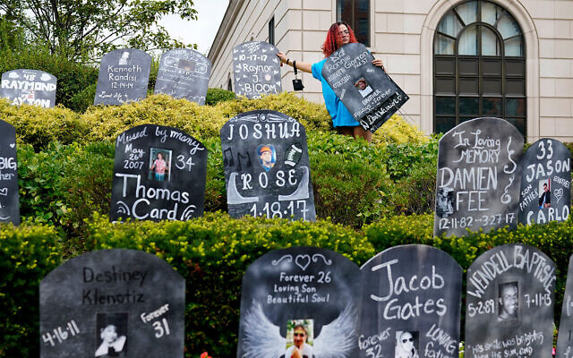 Un militant installant des pierres tombales en carton avec les noms des victimes d'overdose d’opioïdes devant le palais de justice où se déroule le procès de la faillite de Purdue Pharma à White Plains, à New York, le 9 août 2021. (Crédit : AP Photo/Seth Wenig/Dossier)