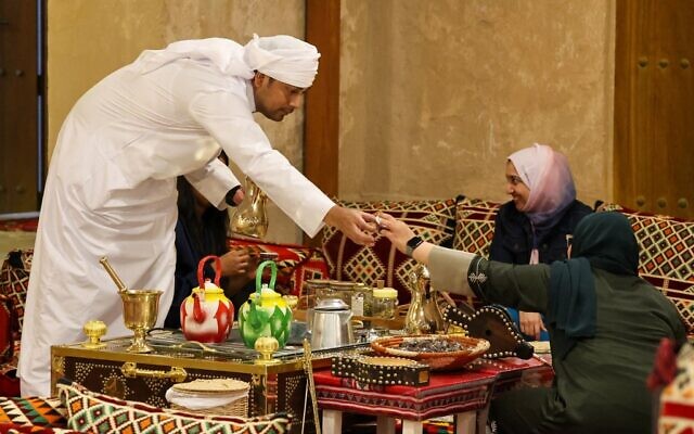 Des visiteurs se voient servir du "gahwa" traditionnel, préparé en torréfiant des grains de café puis en les faisant bouillir avec de la cardamome et du safran, à la maison culturelle Embrace Doha dans le souk al-Wakrah, au sud de la capitale Doha, le 13 septembre 2022. (Crédit : Karim JAAFAR / AFP)
