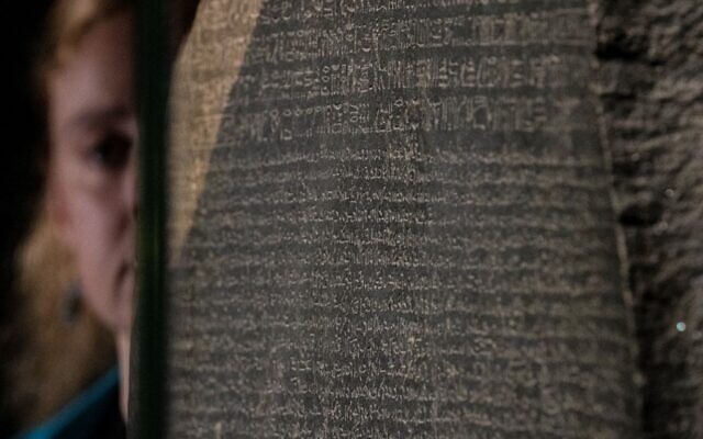 Un employé regarde la pierre de Rosette dans le cadre de l'exposition"Hieroglyphs: unlocking ancient Egypt" au British museum de Londres, le 11 octobre 2022. (Crédit :   CARLOS JASSO / AFP)