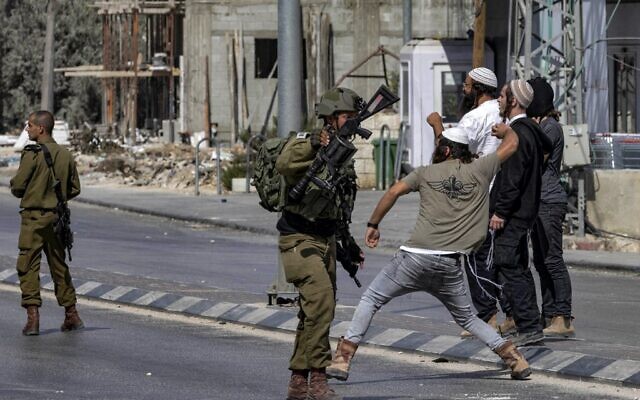 Des soldats israéliens se tiennent à l'écart alors que des Israéliens jettent des pierres sur des Palestiniens lors d'affrontements dans la ville de Huwara en Cisjordanie, le 13 octobre 2022. (Crédit : Oren ZIV / AFP)