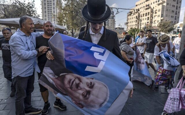 Un Juif ultra-orthodoxe avec une affiche montrant l'ex-Premier ministre israélien et leader du parti du Likud Benjamin Netanyahu pendant un rassemblement de campagne au marché Mahane Yehuda de Jérusalem, le 20 octobre 2022. (Crédit : Menahem Kahana/AFP)