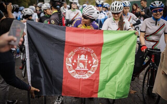 Masomah Ali Zada (C), la première cycliste afghane à participer aux Jeux olympiques en tant que membre de l'équipe de réfugiés du Comité international olympique, attend derrière un drapeau afghan sur la ligne de départ des championnats féminins de cyclisme sur route d'Afghanistan 2022 à Aigle, dans l'ouest de la Suisse, le 23 octobre 2022. (Crédit : VALENTIN FLAURAUD / AFP)