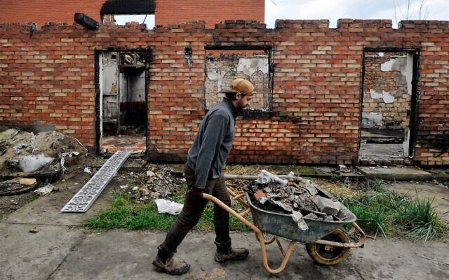 Un volontaire débarrasse les décombres d'une maison détruite à la suite d'un bombardement dans le village de Moshchun, dans la région de Kiev, le 29 octobre 2022, en pleine invasion russe de l'Ukraine. (Crédit : Sergei CHUZAVKOV / AFP)