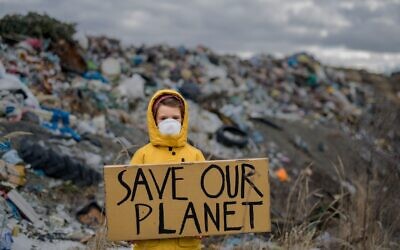 Un enfant se tient sur un site d'enfouissement de déchets avec un appel à sauver notre planète, le 12 juin 2020. (Crédit : Halfpoint/iStock/Getty Images)