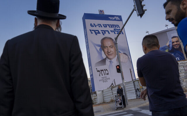 Des personnes passent devant un panneau d'affichage de la campagne électorale, qui affiche Benjamin Netanyahu, ancien Premier ministre israélien et chef du parti Likud et où est écrit en hébreu : "Le 61e siège ne dépend que de vous", à Bnei Brak, une banlieue ultra-orthodoxe de Tel Aviv, le 25 octobre 2022. (Crédit : Oded Balilty/AP)