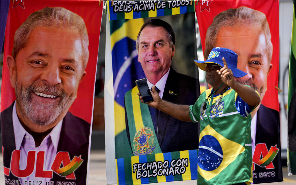 Un manifestant habillé aux couleurs du drapeau brésilien devant un vendeur ambulant de serviettes à l’effigie des candidats à la présidence brésilienne, l'actuel président Jair Bolsonaro, au centre, et l'ancien président Luiz Inacio Lula da Silva, à Brasilia, au Brésil, le 27 septembre 2022. (Crédit : Eraldo Peres/AP) 