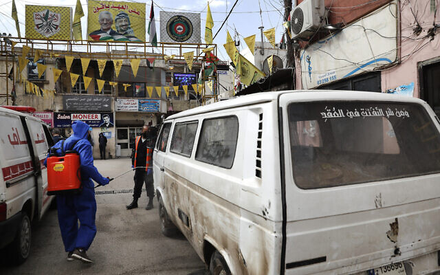 Un travailleur palestinien de l'UNRWA (Agence de secours et de travaux des Nations unies) pulvérise une camionnette, transportant du pain, par précaution contre le coronavirus, à l'entrée fermée de Jalil, ou camp de réfugiés palestiniens de Galilée, à Baalbek, au Liban, le 24 avril 2020. (Crédit : AP Photo/Hussein Malla)