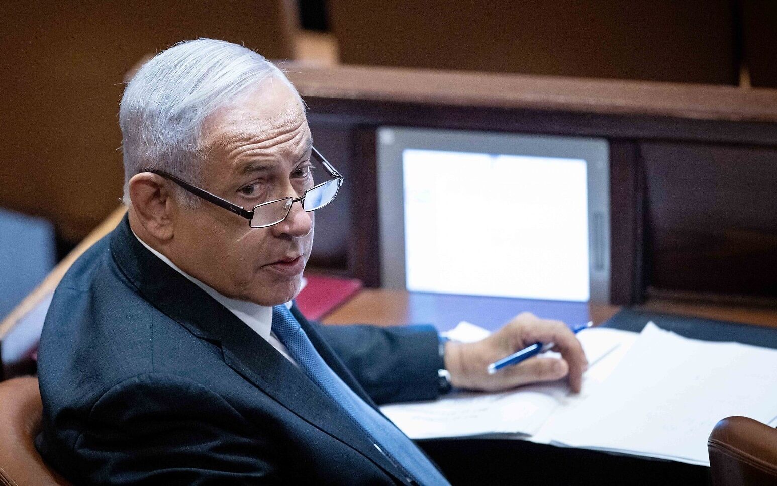 Le chef de l'opposition Benjamin Netanyahu, stylo à la main, à son siège à la Knesset lors d'une session plénière le 11 octobre 2021. (Crédit : Yonatan Sindel/Flash90)