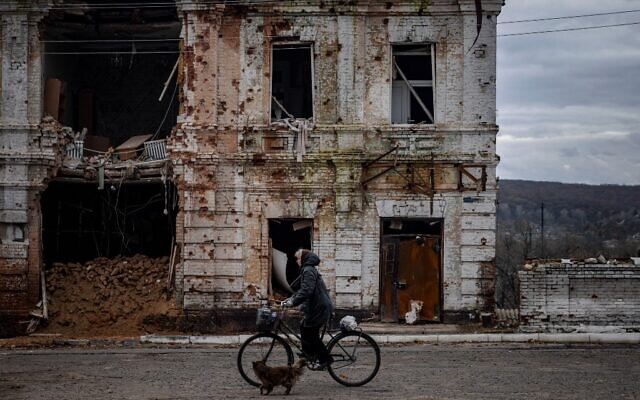 Une femme passe à vélo devant un bâtiment endommagé dans la ville de Kupiansk, le 3 novembre 2022, dans la région de Kharkiv, en pleine invasion russe de l'Ukraine. (Crédit : Dimitar DILKOFF / AFP)