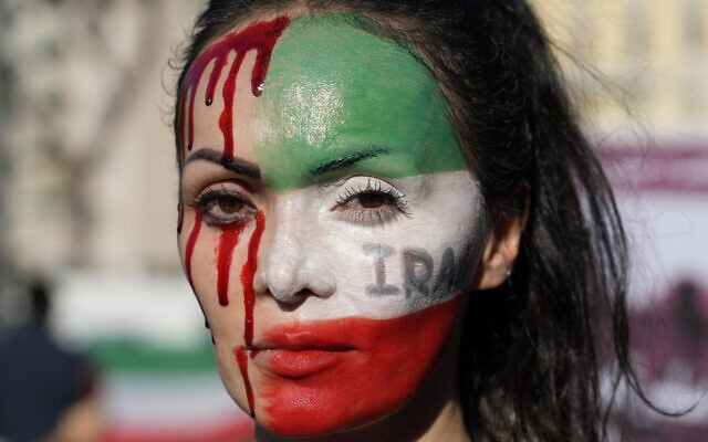 Lors d'un rassemblement dans le centre de Rome, le samedi 29 octobre 2022, une femme dont le visage est scindé en deux : d'un côté du rouge sang qui dégouline et de l'autre le drapeau de l'Iran, en mémoire à la mort de Mahsa Amini, une femme décédée alors qu'elle était en garde à vue en Iran.(Crédit : AP Photo/Gregorio Borgia )