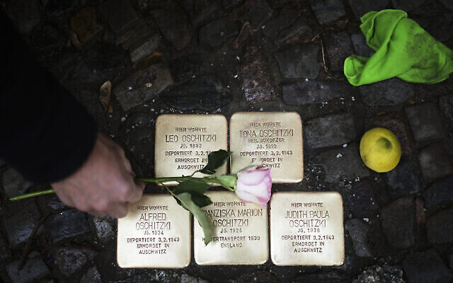 DOSSIER - Un habitant, Juergen Schulz, dépose une fleur après avoir entretenu les « stolpersteines » ou « pavés commémoratifs » installés en mémoire des personnes déportées et tuées par les nazis, devant sa maison à Berlin, en Allemagne, le 9 novembre 2021 (Crédit : AP Photo/Markus Schreiber, dossier)