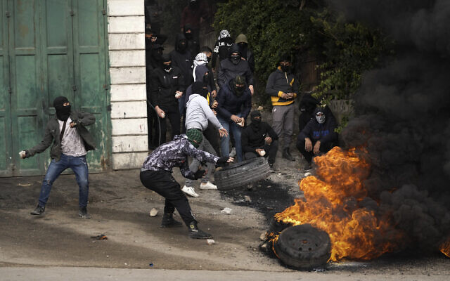 Des Palestiniens masqués brûlent des pneus lors d'affrontements avec les troupes israéliennes après les funérailles de Mufid Khalil dans le village de Beit Ummar, en Cisjordanie, près d'Hébron, le mardi 29 novembre 2022. (Crédit : AP Photo/Mahmoud Illean)