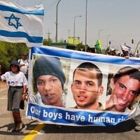 Des manifestants d'Ashkelon défilent avec une banderole en l'honneur du civil israélien captif Avera Mengistu et des soldats décédés Oron Shaul et Hadar Goldin, et arrivent au kibboutz Karmia, le 5 août 2022. (Crédit : Jack Guez/AFP)