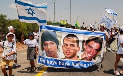 Des manifestants d'Ashkelon défilent avec une banderole en l'honneur du civil israélien captif Avera Mengistu et des soldats décédés Oron Shaul et Hadar Goldin, et arrivent au kibboutz Karmia, le 5 août 2022. (Crédit : Jack Guez/AFP)
