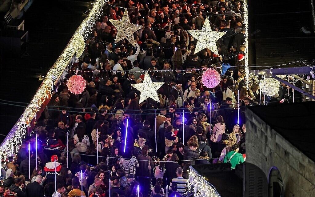 Des fêtards, le 11 décembre 2022, se massent pour assister à la cérémonie d’illumination du sapin de Noël près de la porte Jaffa de la Vieille Ville de Jérusalem. (Crédit : Ahmad Gharabli/AFP)