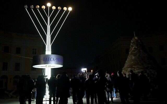 Des membres de la communauté juive se tiennent près d'une hanoukkiah géante lors d'ne cérémonie pour la fête juive de Hanoukka dans la ville ukrainienne d'Odessa, pendant une panne d'électricité, le 18 décembre 2022, lors de l'invasion russe de l'Ukraine. (Crédit : Oleksandr GIMANOV / AFP)