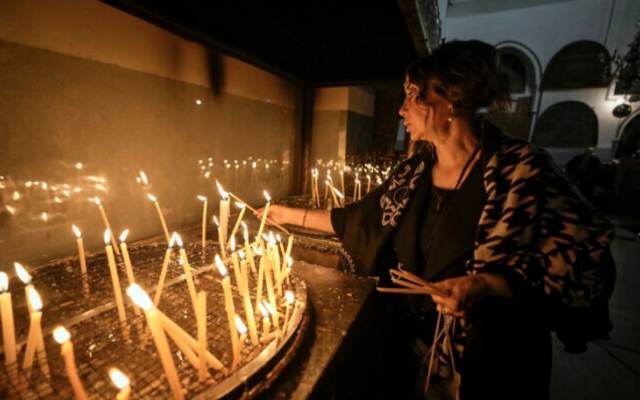 Une femme allumant des bougies dans l'église de la Nativité, traditionnellement considérée comme le lieu de naissance de Jésus Christ, à Bethléem, en Cisjordanie, le 24 décembre 2022. (Crédit : AP Photo/Majdi Mohammed)