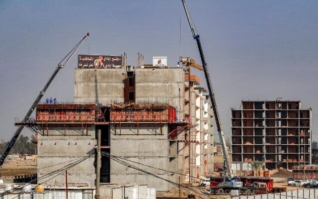 Des ouvriers de la construction se tiennent sous une grue au sommet d'un immeuble d'habitation inachevé dans la capitale irakienne, Bagdad, le 16 décembre 2022. (Crédit : AHMAD AL-RUBAYE / AFP)
