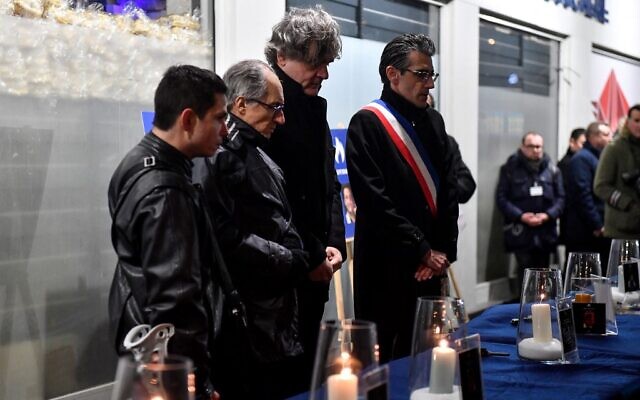 Riss (3e à gauche), caricaturiste français de « Charlie Hebdo », se tient à côté d'une bougie allumée pour les victimes lors d'une cérémonie commémorative marquant le 8e anniversaire de l'attaque terroriste islamiste meurtrière de 2015 contre le supermarché juif Hyper Cacher à Paris, le 9 janvier 2023. (Crédit : JULIEN DE ROSA / AFP)
