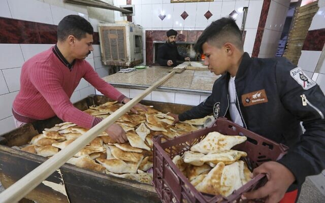 Un jeune Irakien achète des pains fraîchement cuits dans une boulangerie de pain Samoun dans la rue al-Rashid, à Bagdad, la capitale de l'Irak, le 11 janvier 2023. (Crédit : Sabah ARAR / AFP)