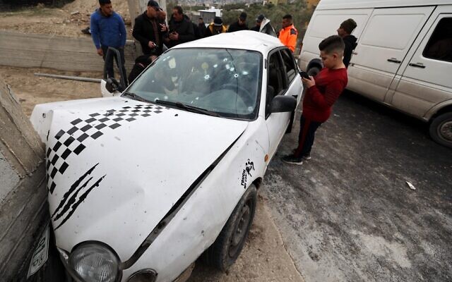 Des passants autour d'une voiture criblée de balles où circulaient deux membres du Jihad islamique palestinien qui ont été tués par les soldats israéliens à Jaba, près de Jénine, en Cisjordanie, le 14 janvier 2023. (Crédit : Jaafar Ashtiyeh/AFP)