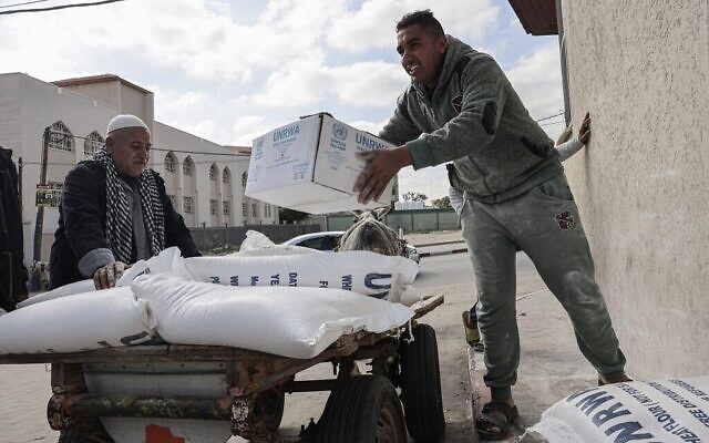 Des Palestiniens portent des sacs de farine et d'autres produits alimentaires de base reçus comme aide aux familles pauvres, au centre de distribution de l'Office de secours et de travaux des Nations Unies pour les réfugiés de Palestine (UNRWA), dans le camp de réfugiés de Rafah, dans le sud de la bande de Gaza, le 22 janvier 2023. (Crédit : SAID KHATIB / AFP)