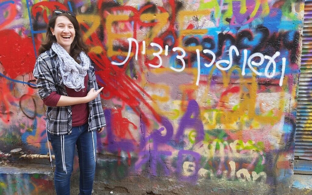 Rachel Schwartz se tient devant un morceau de graffiti qui joue sur le commandement de porter des tzitzit, écrit au féminin en hébreu. (Crédit : Autorisation de Rachel Schwartz/JTA)