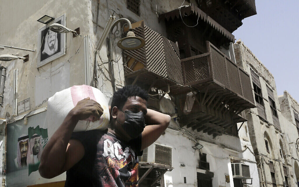 Un ouvrier, portant un masque facial par mesure de précaution contre le coronavirus, porte une charge dans le district historique de Djeddah, à Djedda, en Arabie saoudite, le 15 juin 2020. (Crédit : AP Photo/Amr Nabil)