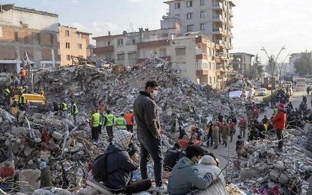 Des personnes se tiennent au-dessus des décombres de bâtiments effondrés pendant les opérations de sauvetage après qu'un tremblement de terre de magnitude 7,8 a frappé la région frontalière de la Turquie et de la Syrie la semaine dernière, à Hatay, en Turquie, le 12 février 2023. (Crédit : BULENT KILIC/AFP)