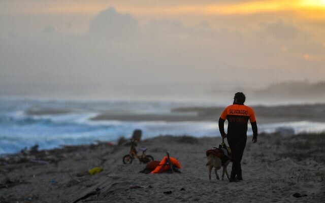 Un membre de la police cynophile et son chien patrouillent le 26 février 2023 sur la plage de Steccato di Cutro, au sud de Crotone, en Italie, où les débris d'un bateau ont été rejetés après le naufrage d’une navigation de migrants au large du sud de la Calabre. (Crédit : Alessandro SERRANO / AFP)