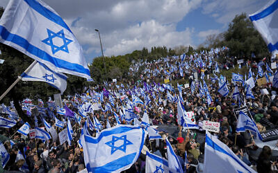Des Israéliens agitant des drapeaux lors d'une manifestation contre les projets du gouvernement du Premier ministre Benjamin Netanyahu de remanier le système judiciaire, devant la Knesset à Jérusalem, le 13 février 2023 (Crédit : Ohad Zwigenberg/AP)