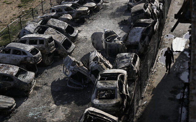  Un Palestinien marchant près de voitures brûlées, dont certaines ont été retirées de la route pour être remplacées par des pièces détachées, dans la ville de Huwara, près de la ville de Naplouse en Cisjordanie, le 27 février 2023. (Crédit : AP Photo/Majdi Mohammed)