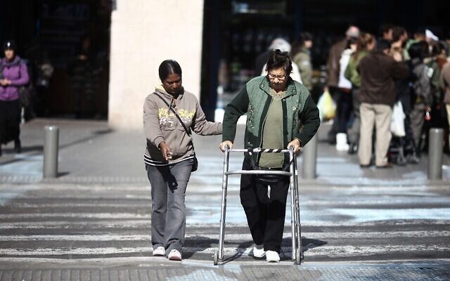Un soignant aide un Israélien âgé à traverser la rue à Tel Aviv. Illustration (Crédit : Kobi Gideon/Flash90)