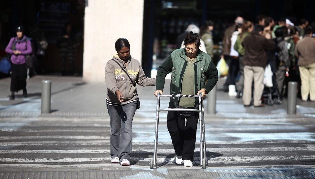 Illustration : Une soignante aidant une personne âgée israélienne à traverser la rue, à Tel Aviv. (Crédit : Kobi Gideon/Flash90)
