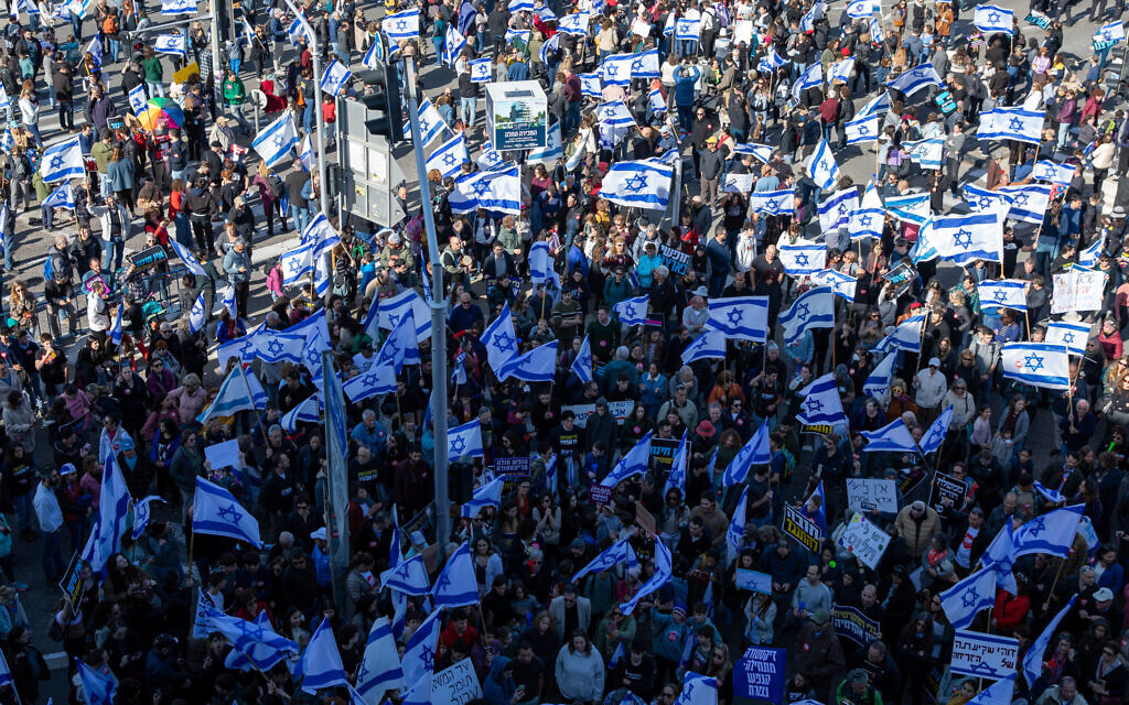 Des milliers d'Israéliens tiennent des pancartes et agitent le drapeau israélien alors qu'ils marchent dans les rues de Haïfa, pour protester contre le remaniement judiciaire prévu par le gouvernement israélien, le 20 février 2023. (Crédit : Shir Torem/Flash90)