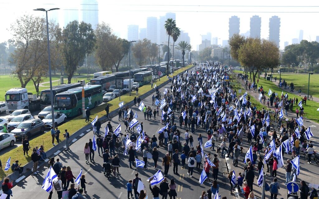 Des milliers d'Israéliens tiennent des pancartes et agitent le drapeau israélien alors qu'ils marchent dans les rues de Tel Aviv, pour protester contre le remaniement judiciaire prévu par le gouvernement israélien, le 20 février 2023. (Crédit : Tomer Neuberg/FLASH90)