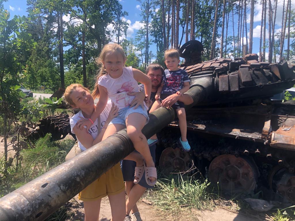 Olesei (L) et Ruslan posent avec leurs enfants devant un char russe détruit à l'extérieur de Kiev, le 22 juillet 2022.(Crédit : Lazar Berman/The Times of Israel)