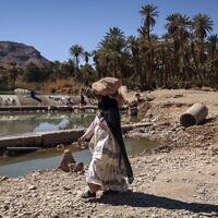 Une femme passe devant un étang dans le village de Tagadirt, dans la région oasis de Tata au Maroc, le 28 février 2023. (Crédit : FADEL SENNA / AFP)