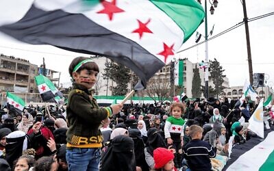 Un petit garçon brandit un drapeau syrien pendant un rassemblement marquant le douzième anniversaire du début du soulèvement contre le président Bashar El-Assad et son gouvernement à Idlib, ville du nord-ouest de la Syrie détenue par les rebelles, le 15 mars 2023. (Crédit :OMAR HAJ KADOUR / AFP)
