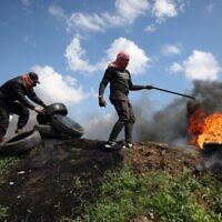 Des manifestants palestiniens brûlant des pneus lors d'une petite manifestation à l'appel du Hamas contre le sommet régional de Charm el-Cheikh, en Égypte, à l'est de la ville de Gaza, près de la frontière avec Israël, le 19 mars 2023. (Crédit : Mahmud Hams/AFP)