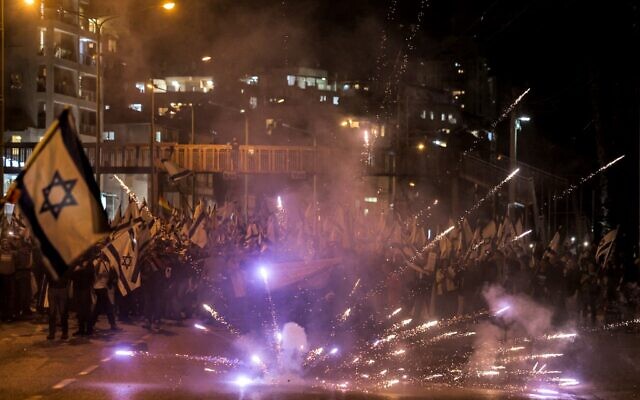 Des feux d'artifice explosent devant des manifestants qui défilent contre le projet de loi de réforme judiciaire du gouvernement, à Bnei Barak, le 23 mars 2023. (Crédit : Ahmad Gharabli/AFP)