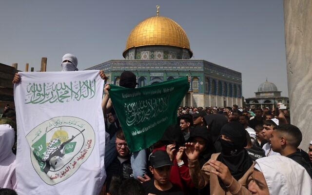 Des personnes brandissent une bannière (à gauche) portant le logo des Brigades Ezzedine al-Qassam, l'aile militaire du Hamas, après la première prière du vendredi midi du mois de jeûne islamique du Ramadan, devant le sanctuaire du Dôme du Rocher dans l'enceinte de la mosquée Al-Aqsa à Jérusalem, le 24 mars 2023. (Crédit : AHMAD GHARABLI / AFP)