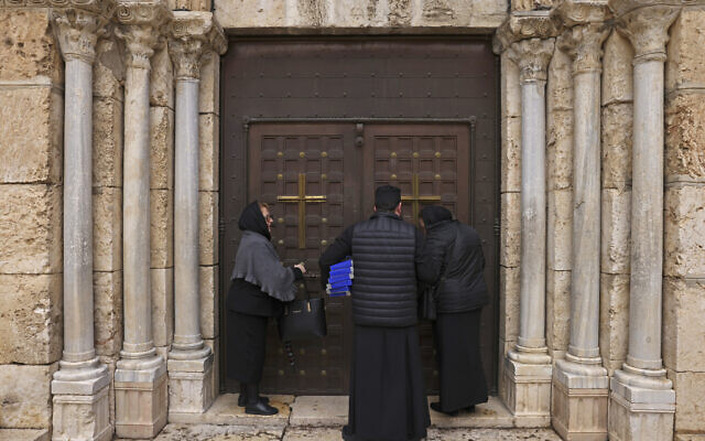 Des fidèles se tiennent avec un moine devant l'entrée fermée du tombeau de la Vierge Marie à Jérusalem suite à l'agression présumée d'un prêtre, le 19 mars 2023. (Crédit : HAZEM BADER / AFP)
