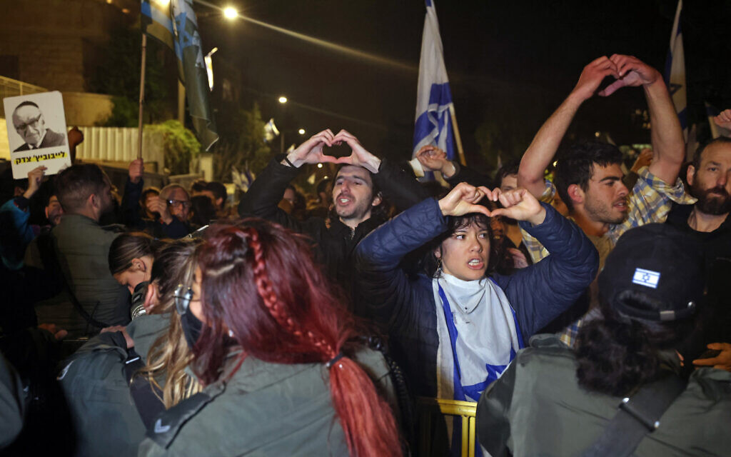 Des manifestants agitent des drapeaux nationaux lors d'un rassemblement contre les réformes judiciaires du gouvernement israélien devant la résidence du Premier ministre Benjamin Netanyahu à Jérusalem, le 27 mars 2023. (Crédit : AHMAD GHARABLI / AFP)