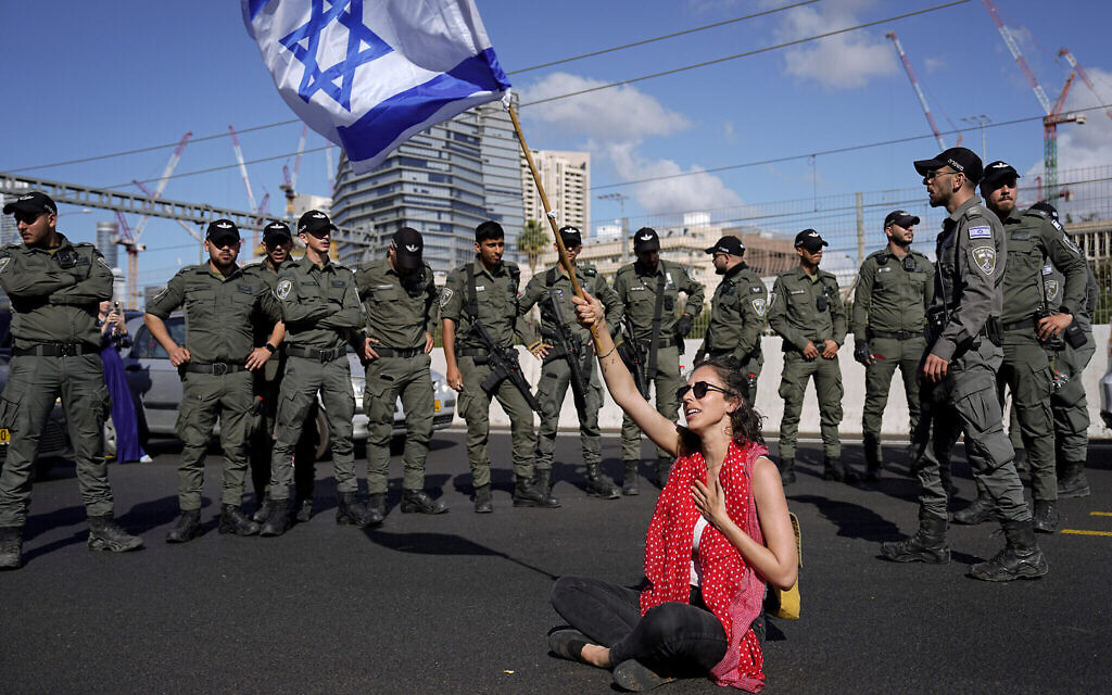 Une manifestante brandissant le drapeau israélien, assise sur une autoroute et encadrée par la police des frontières, lors d'une manifestation contre les projets du gouvernement du Premier ministre Benjamin Netanyahu de remanier le système judiciaire, à Tel Aviv, Israël, le 9 mars 2023. (Crédit : AP Photo/Ariel Schalit)