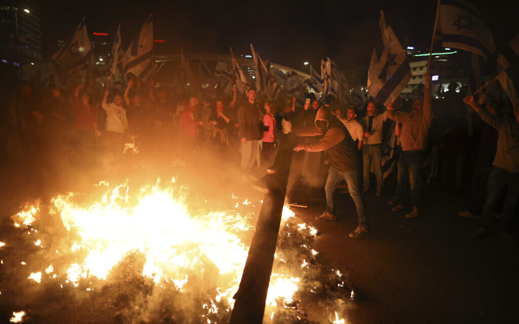 Des Israéliens opposés au plan de réforme judiciaire du Premier ministre Benjamin Netanyahu allument des feux de joie et bloquent une autoroute lors d'une manifestation quelques instants après que le dirigeant israélien a limogé son ministre de la Défense, à Tel Aviv, Israël, le 26 mars 2023. (Crédit : AP Photo/Oren Ziv)