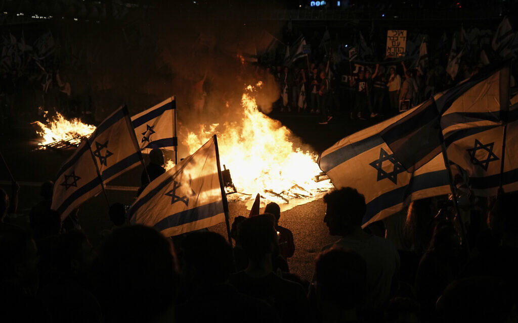 Des Israéliens opposés au plan de réforme du système judiciaire du Premier ministre Benjamin Netanyahu allumant des feux de joie et bloquant une autoroute lors d'une manifestation quelques instants après que le dirigeant israélien a limogé son ministre de la Défense, à Tel Aviv, en Israël, le 26 mars 2023. (Crédit : AP Photo/Ohad Zwigenberg)
