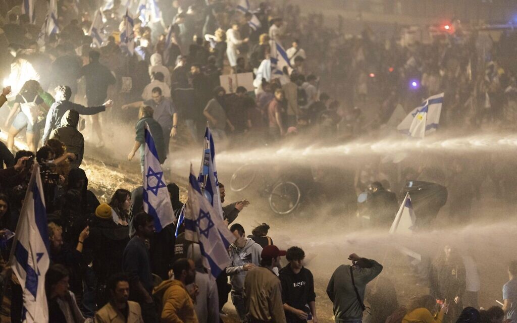 La police israélienne utilise un canon à eau pour disperser les manifestants qui bloquent une autoroute lors d'une manifestation contre les plans du gouvernement du Premier ministre Benjamin Netanyahu visant à réformer le système judiciaire à Tel Aviv, Israël, le 27 mars 2023. (Crédit : AP Photo/Oren Ziv)