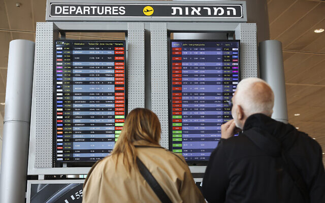 Des passagers regardant un écran affichant les vols retardés à l'aéroport Ben Gurion, le 27 mars 2023. (Crédit : AP Photo/Oren Ziv)