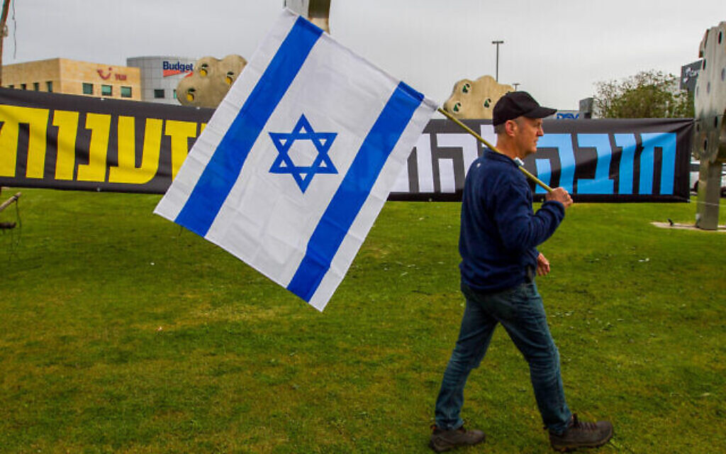 Un Israélien brandit un drapeau d'Israël lors d'une manifestation contre les membres de la coalition et la refonte judiciaire prévue à Airport City, le 22 mars 2023. (Crédit : Flash90)